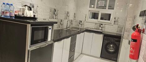A modern kitchen with a microwave, sink, and dishwasher. There is a fire extinguisher mounted on the wall.
