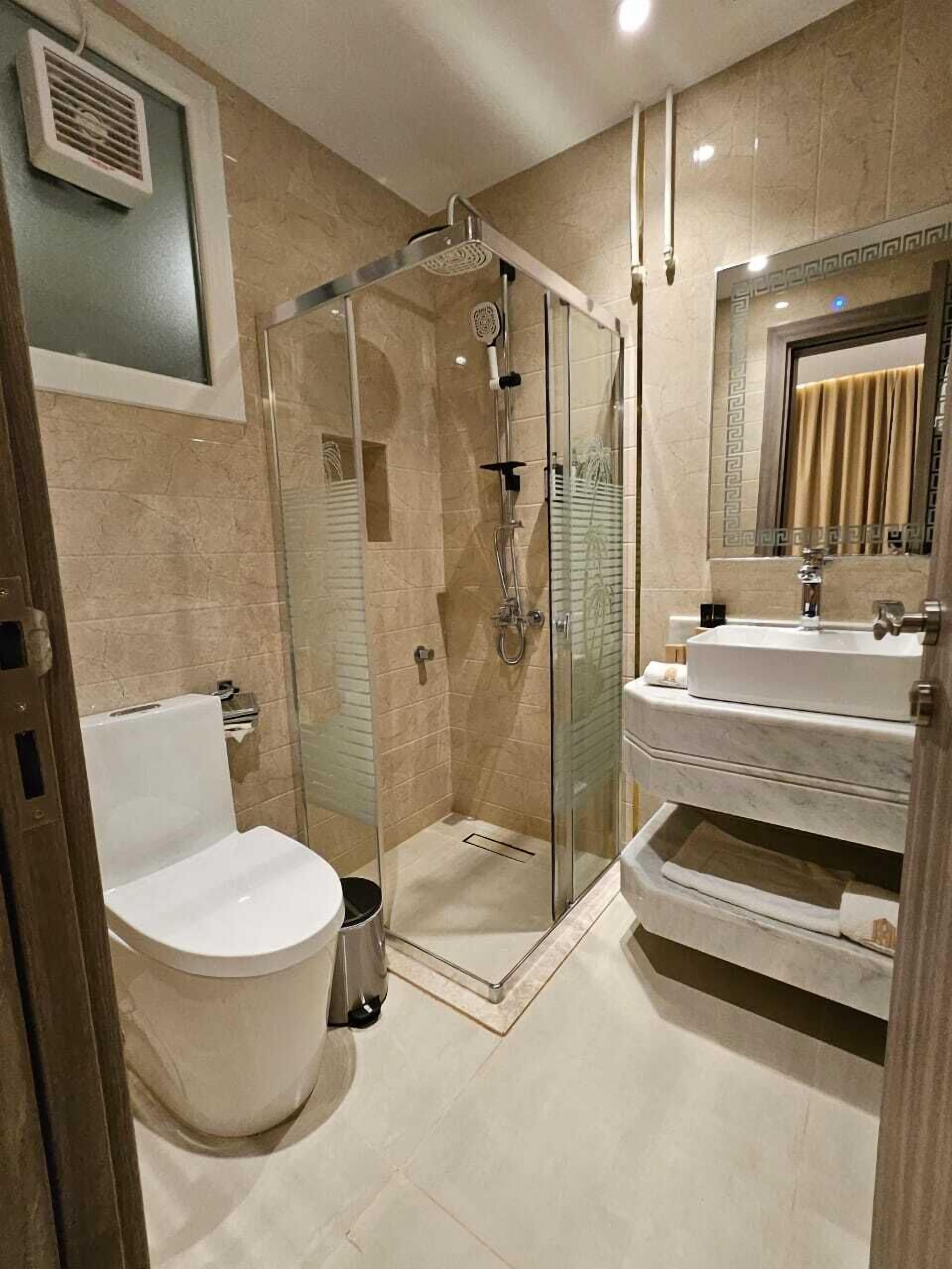 A modern bathroom with a glass-enclosed shower, a white toilet, and a vanity with a mirror and towel rack.