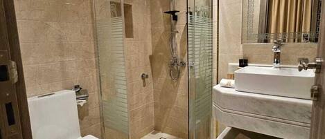 A modern bathroom with a glass-enclosed shower, a white toilet, and a vanity with a mirror and towel rack.