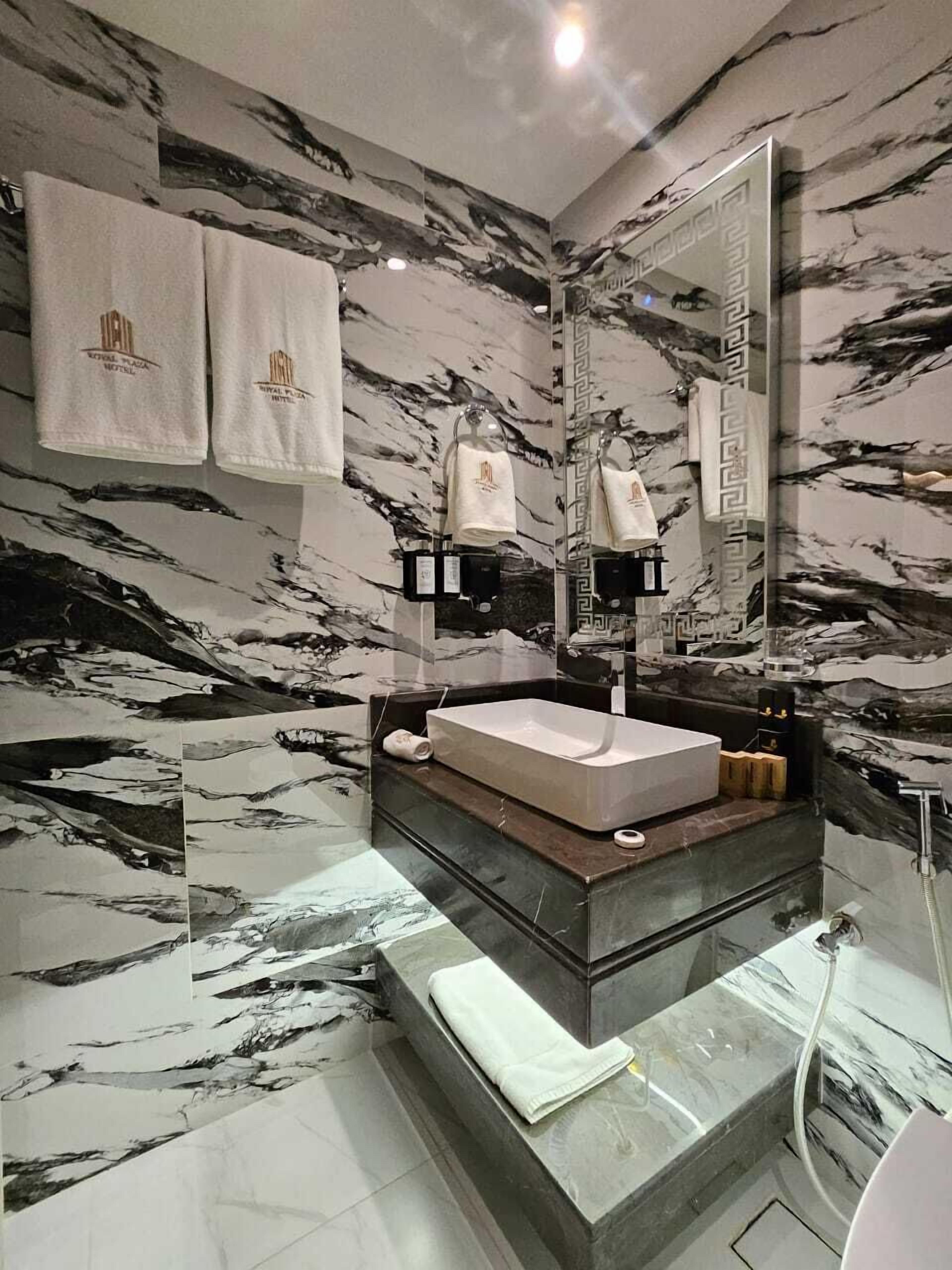 Un baño moderno con tocador de mármol, un espejo grande y dos toallas colgadas en la pared.
