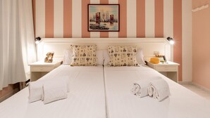 Habitación de hotel con paredes a rayas, una cama con sábanas blancas, dos mesitas de noche con lámparas y un cuadro de un puente.