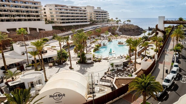 Un hotel con piscina, palmeras y vista al océano.