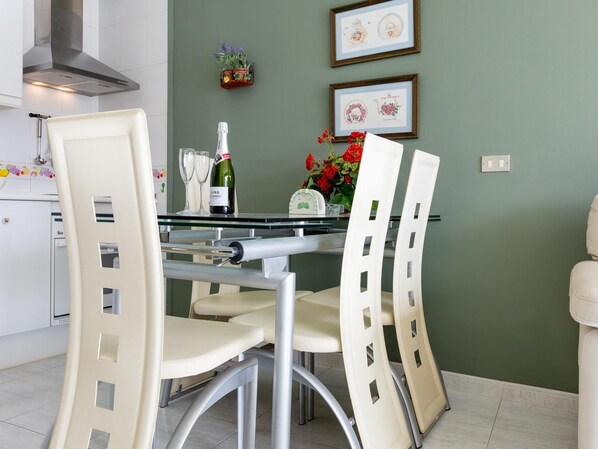 Une cuisine moderne avec des chaises blanches, une table en verre et une bouteille de vin.