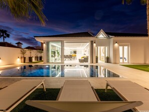 Ein modernes Haus mit Swimmingpool, einer Terrasse mit Liegestühlen und einem hellen Innenraum.