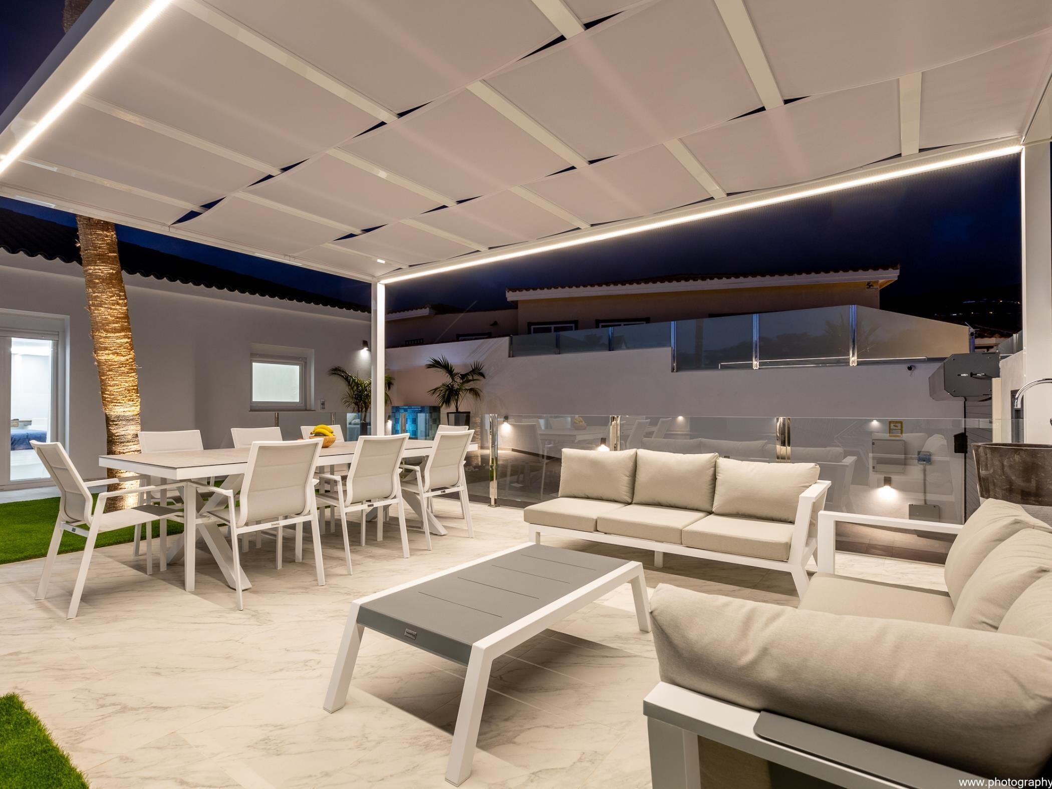Un espacio exterior moderno para disfrutar al aire libre, con una mesa de comedor, sillas, un sofá y una mesa de centro.