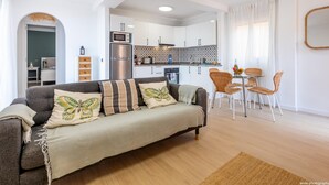 A modern living room with a sofa, a dining area with wicker chairs, a kitchen with white cabinets, and a large mirror on the wall. - Salt and Sea Apartment, Sea View, Free Wi Fi (Costa Adeje)