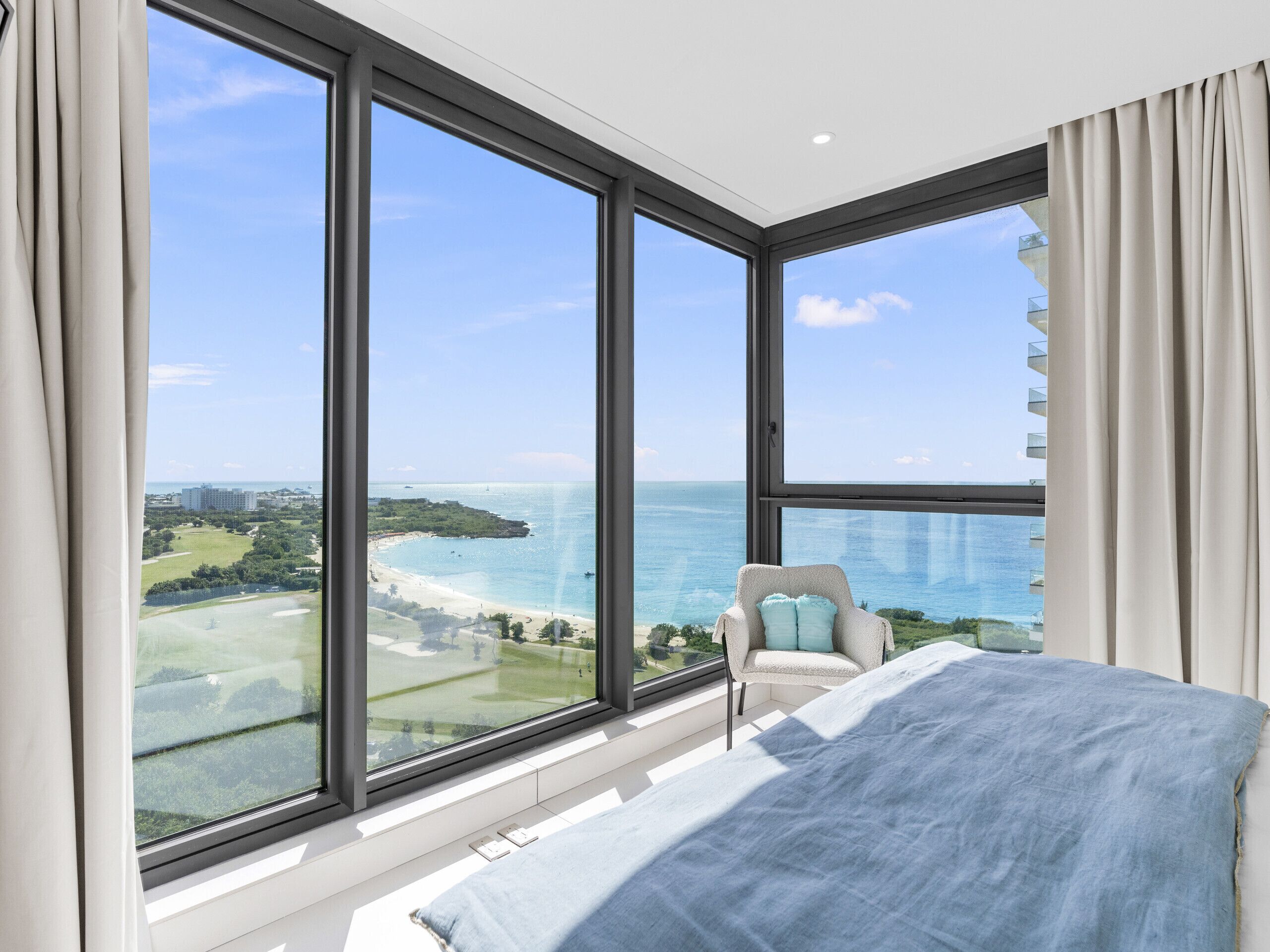 A bedroom with large windows offering a view of a beach and ocean.
