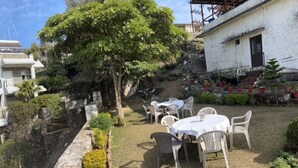 A garden with a white building, outdoor seating, and a tree. - Hotel Mansarovar (Abu Road)
