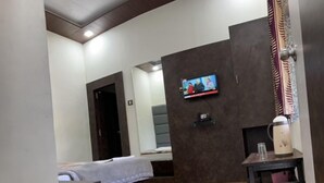 A hotel room with a bed, a TV mounted on the wall, a coffee maker on a table, and a wooden floor. - Hotel Mansarovar (Abu Road)