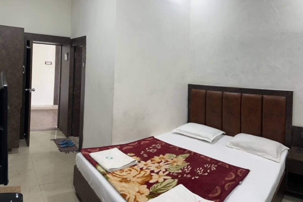 A hotel room with a bed, a wooden headboard, a door, and a hallway.