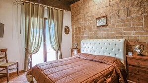 A bedroom with a brick wall, a bed with a tufted headboard, a wooden dresser, a chair, and a nightstand with a lamp. - Gorgeous home in Realmonte with WiFi (Realmonte)