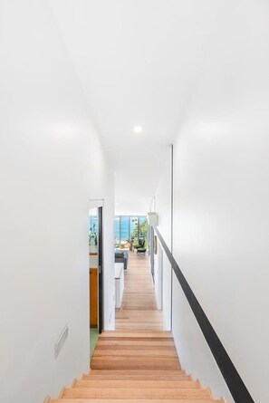 A modern interior with a wooden staircase leading to a bright room with a view. - Sandcastle by Coast Hosting (Forresters Beach)