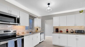 Een moderne keuken met witte kastjes, roestvrijstalen apparatuur en een betegelde achterwand.