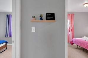 Une chambre à coucher avec un lit, une table de chevet, une étagère avec une pancarte et un rideau.