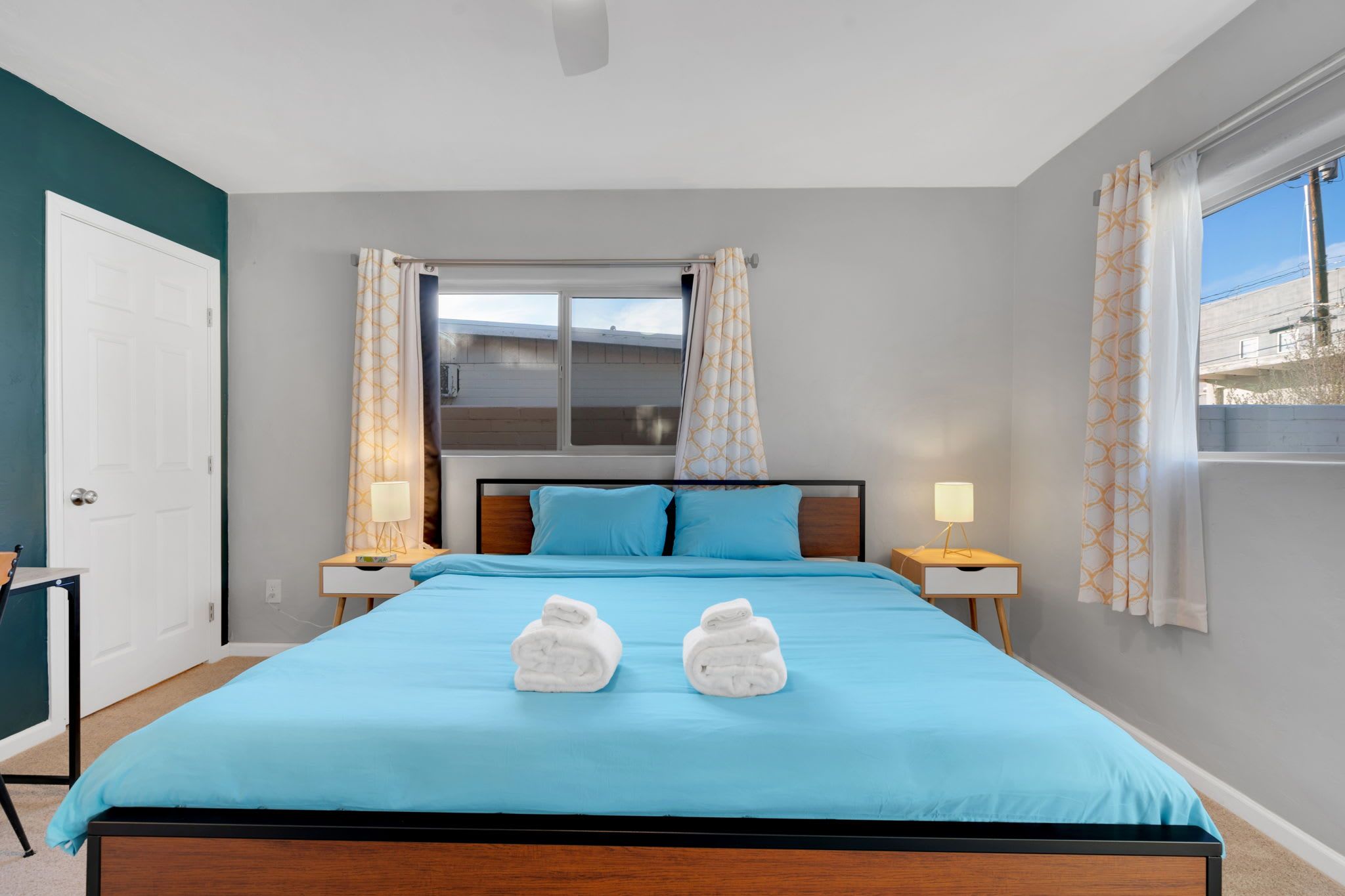 Una habitación de hotel con cama, dos lámparas de noche, ventana con cortinas y vistas al exterior.