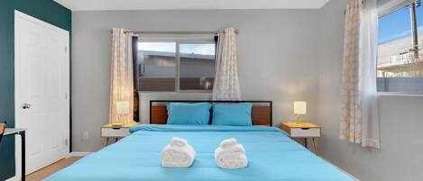 Una habitación de hotel con cama, dos lámparas de noche, ventana con cortinas y vistas al exterior.