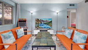 Een woonkamer met twee oranje banken, een salontafel, een grote televisie en een retro gameconsole.