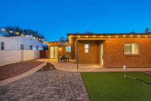 A backyard with a patio, a brick building, and a small artificial green area. - The Swing by Velo (Tucson)