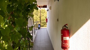 Un pasillo con extintor fijado en la pared, suelo de baldosas y barandilla a un lado.