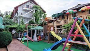 Un parque infantil con toboganes y columpios, un sendero de ladrillos y un edificio con balcón al fondo.