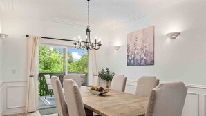 Une salle à manger avec une table en bois, six chaises, un lustre et un tableau accroché au mur.
