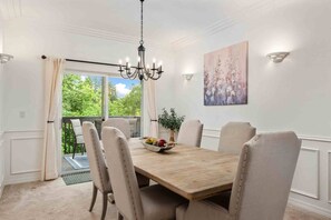 A dining room with a wooden table, six chairs, a chandelier, and a painting on the wall.