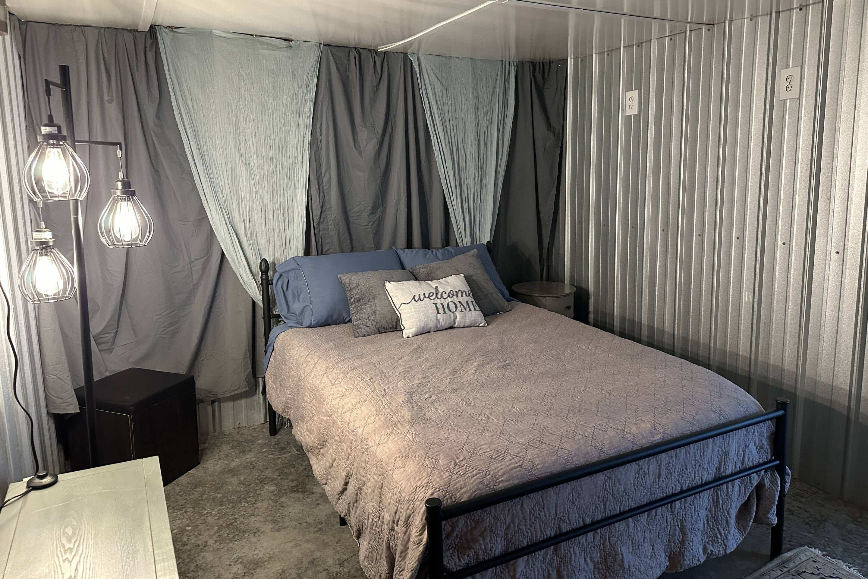 Un dormitorio con cama, mesita de noche, lámpara y cortinas.