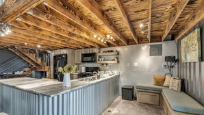 A kitchen with a wooden ceiling, a marble countertop, and a built-in bench with cushions.