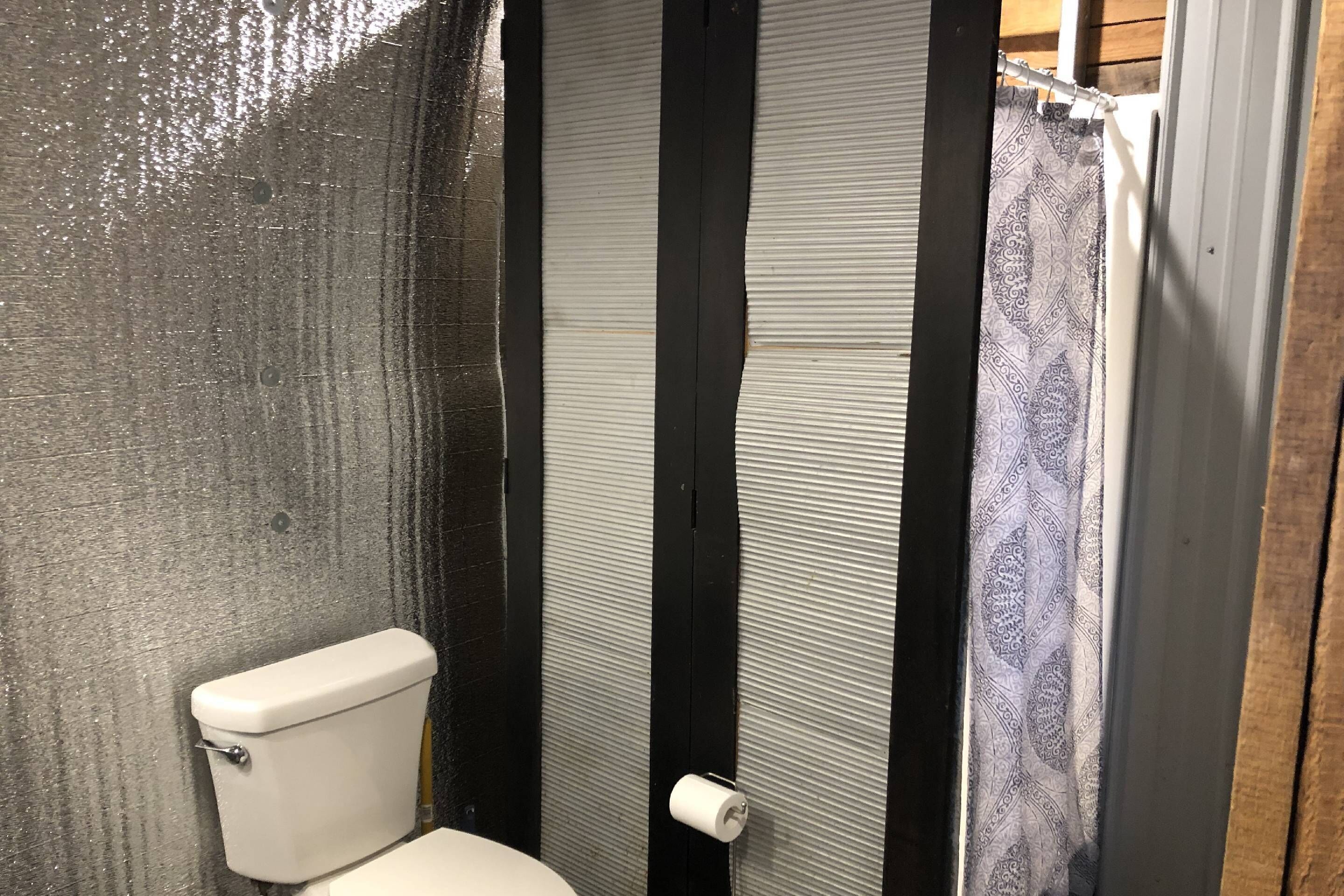 Une salle de bain avec des toilettes, un rideau de douche et un mur à texture.