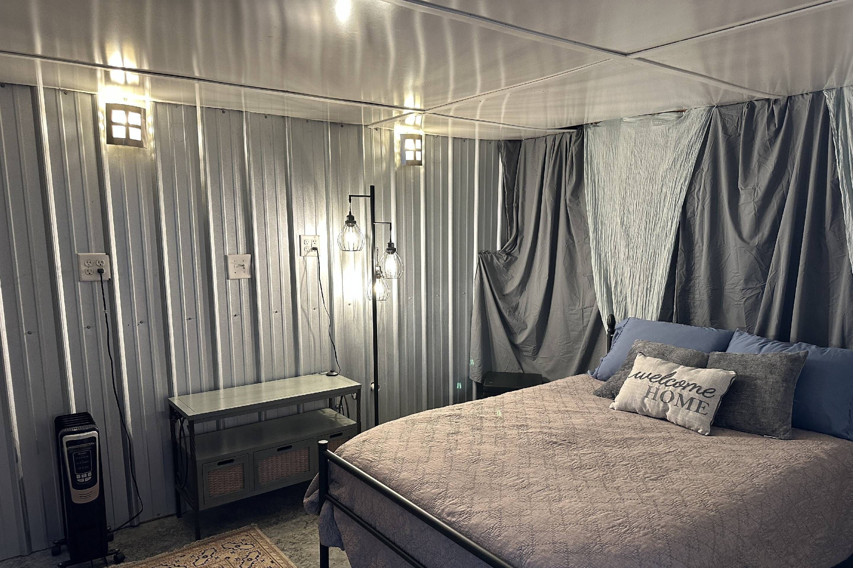 A bedroom with a bed, bedside table, lamp, and curtains.