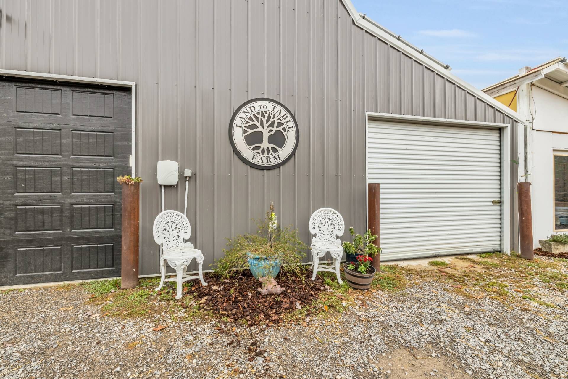 A building with a large garage door, two white chairs, and a circular sign with a tree design.