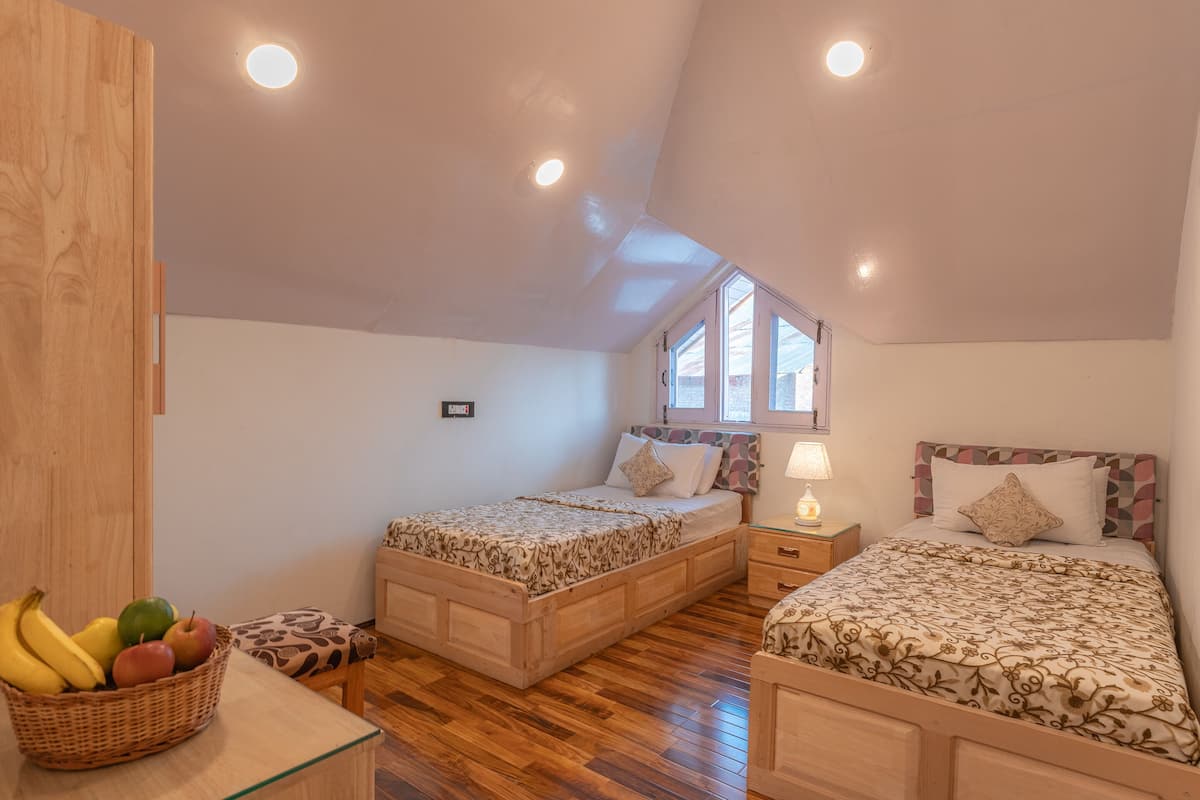 A bedroom with two wooden beds, a nightstand, a lamp, a wooden wardrobe, and a fruit basket.
