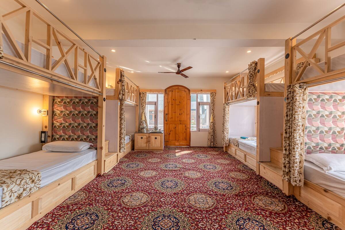 A room with bunk beds, a patterned carpet, a wooden door, and a ceiling fan.