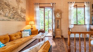 A cozy room with a sofa, a table, a clock, and a view of greenery outside.