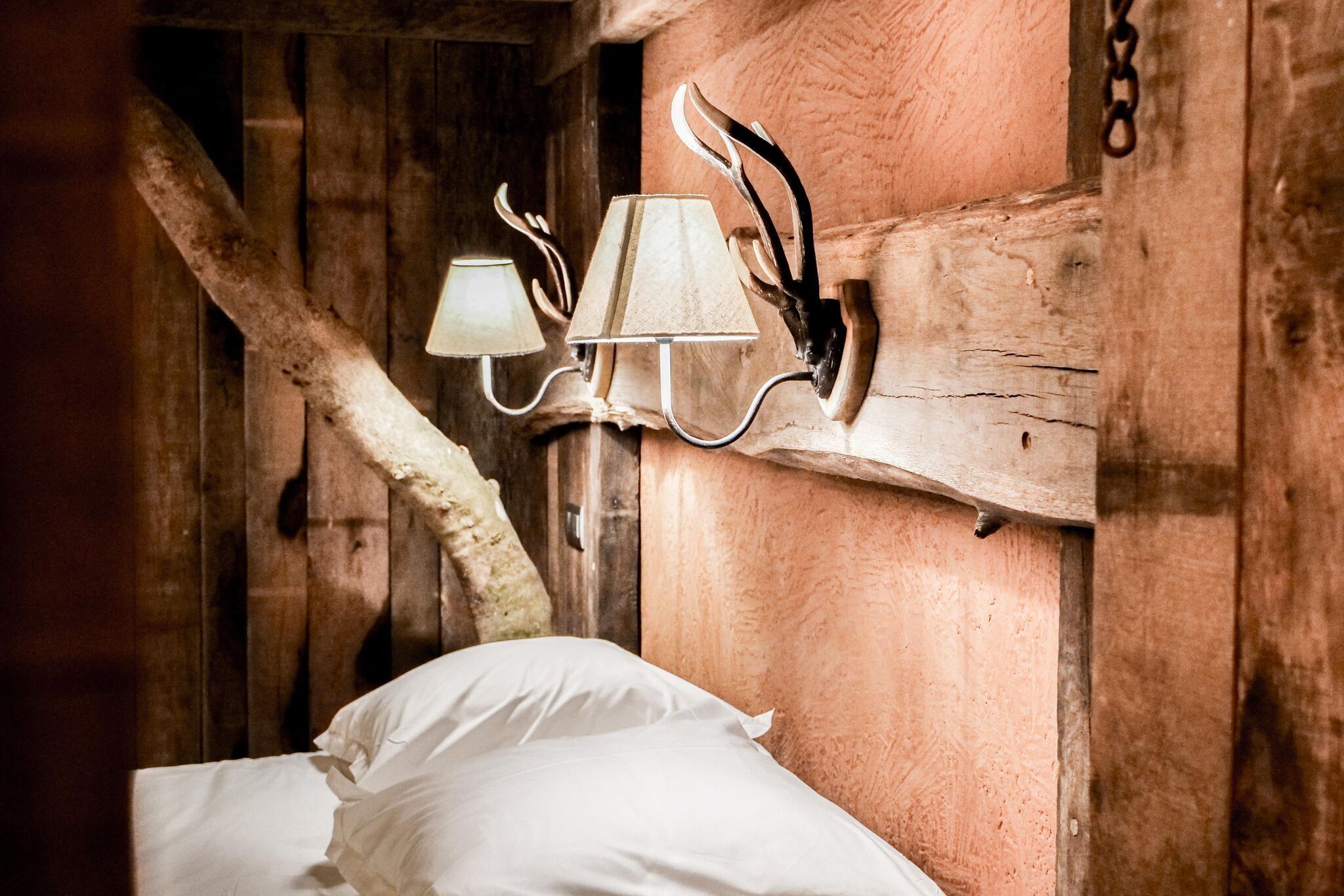 Una habitación rústica de madera con una cama, una lámpara de pared con una cabeza de ciervo y una viga de madera.