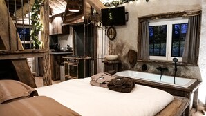 A rustic bedroom with a large bed, a wooden bench, a sink, and a window with curtains. - Spacious holiday home in the woods (Bastogne)
