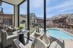 A modern hotel room with large windows, a pool, and a mountain view.
