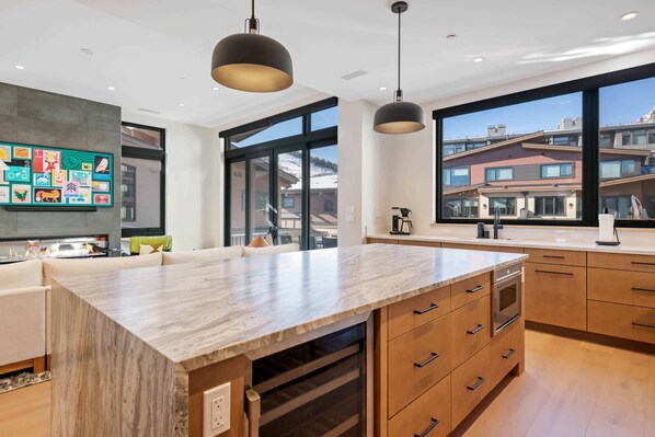 A modern kitchen with a large island, wooden cabinets, and pendant lighting.