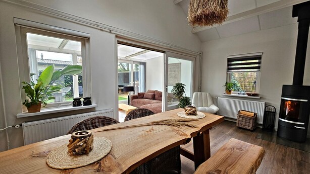 A spacious living area with a wooden dining table, wicker chairs, and a large window offering a view of the outdoors.
