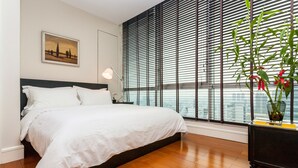 Un dormitorio con una cama grande, una mesita de noche, una lámpara, una ventana con persianas y una planta en maceta.