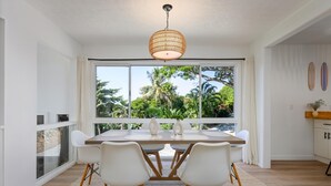 Un comedor con un ventanal grande, sillas blancas, una mesa de madera y una lámpara colgante.