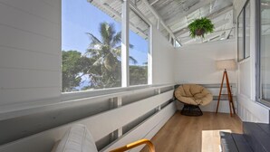 Una habitación con un ventanal grande, suelo de madera, un banco acolchado blanco, una silla de madera y una lámpara de pie.