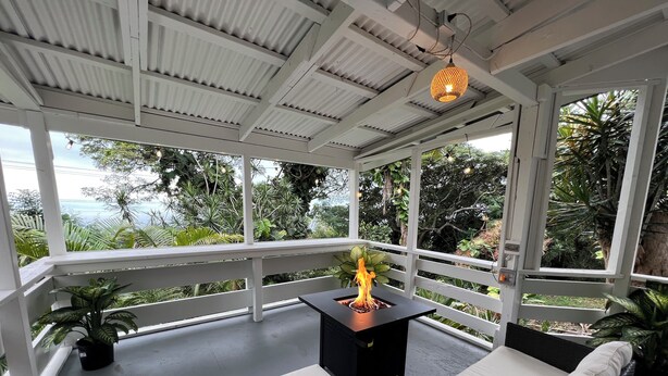 Un área de estar al aire libre con techo, una chimenea, asientos blancos acolchados y plantas en macetas.