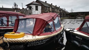 A row of moored boats with a house in the background. - Rhif Deg (Brecon)