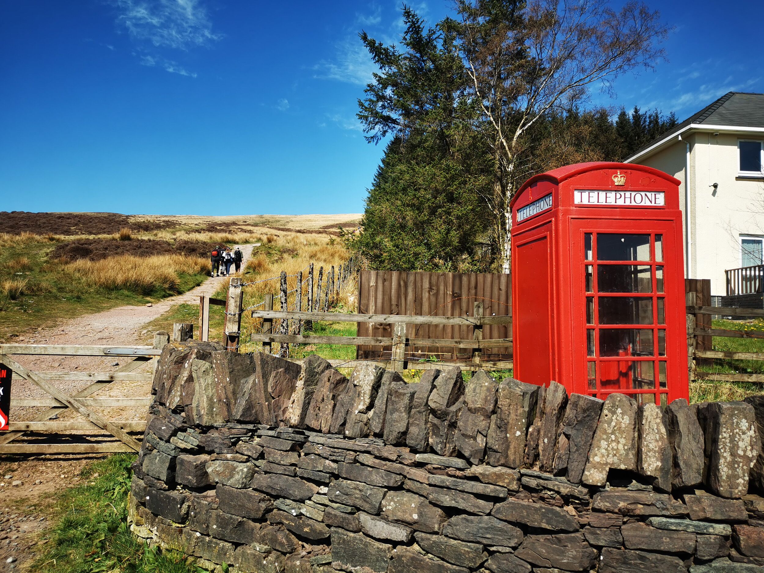 A red telephone booth, a stone wall, and a path leading to a building.