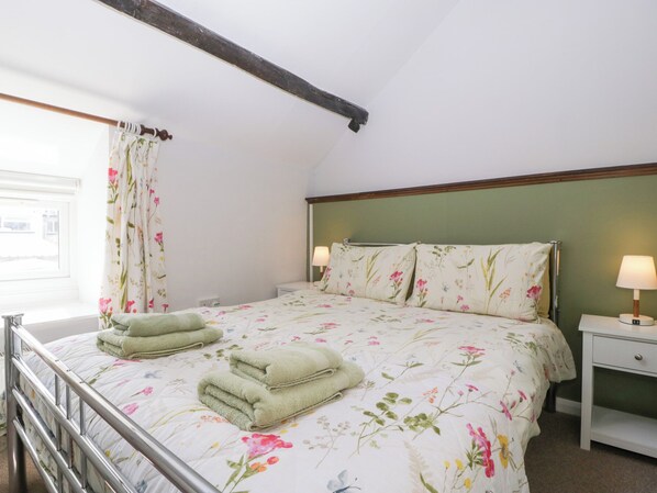 Un dormitorio con cama, dos mesitas de noche, una ventana con cortinas y una viga de madera en el techo.