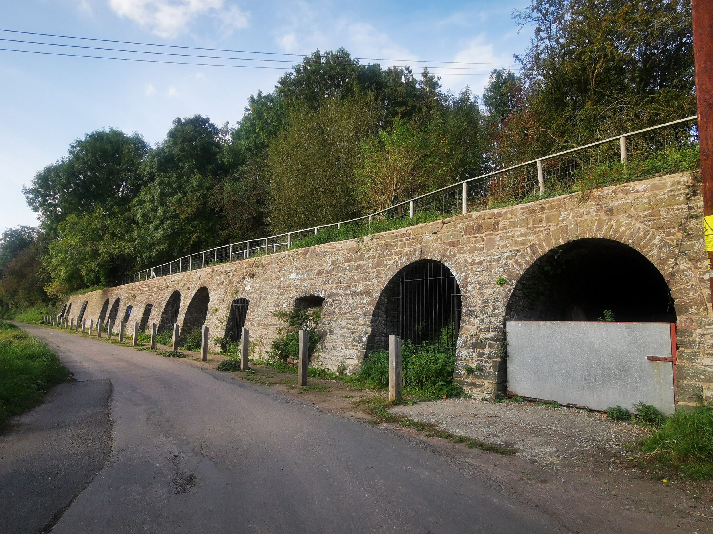 Un puente de piedra con varios arcos sobre una carretera, rodeado de vegetación.