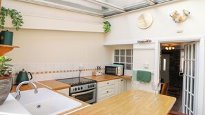 A modern kitchen with a wooden countertop, a sink, a stove, and a microwave. There is a window above the sink and a door leading to another room. - Rhif Deg (Brecon)