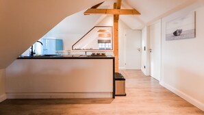 A modern kitchen with a central island, wooden beams on the ceiling, and a view into an adjacent room. - Appartement Wattside (Morsum)