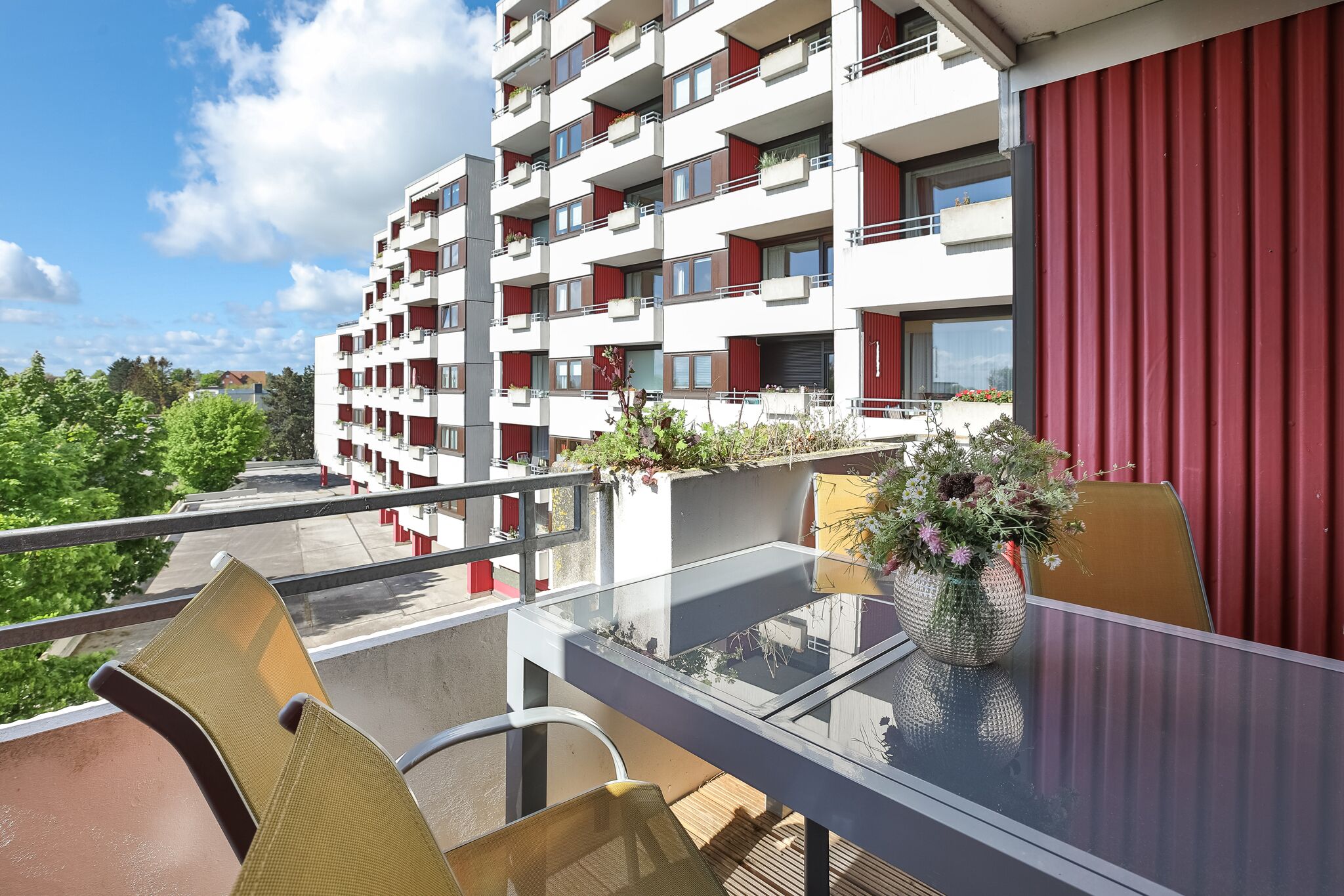 En modern lägenhetsbyggnad med balkonger, ett bord i glas och utomhusmöbler.